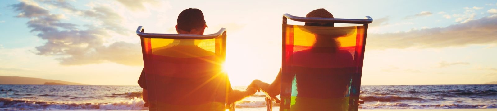 couple sitting in beach chairs on the beach watching the sunset