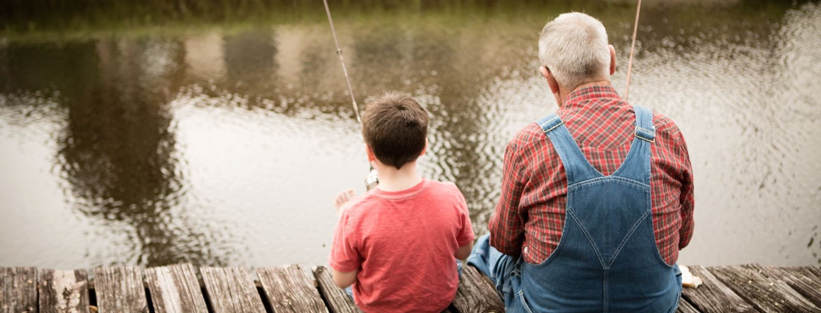 elderly man and young boy sitting on a dock fishing in a pond